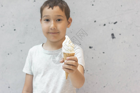 8岁的男孩将香草冰淇淋放在华夫饼蛋卷里灰色背景图片