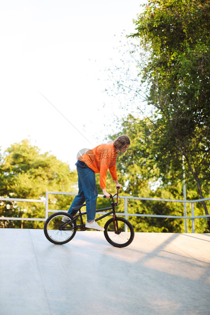 穿着橙色拖车的酷小帅哥骑自行车在现代滑图片