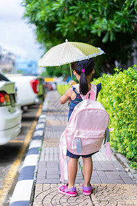 带着雨伞和背包的小女孩在公园里走着图片