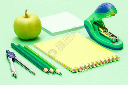 指南针彩色铅笔记本苹果纸条和绿色背景的订书机图片