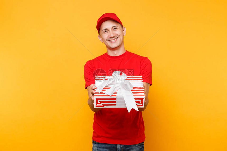 穿着红色制服的送货员在黄橙色背景下被隔离戴着帽子T恤作为快递员或经销商拿着红色礼盒的专业微笑男员工服务理图片