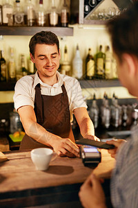 顾客在咖啡馆用手机付款有支付终端的酒保在酒吧柜图片