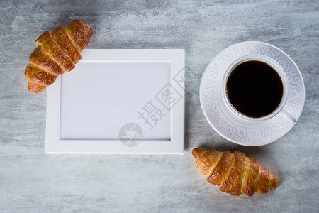 空白的色框架与副本空间杯咖啡和灰色桌子背景上的羊角面包带有复制空间的图片