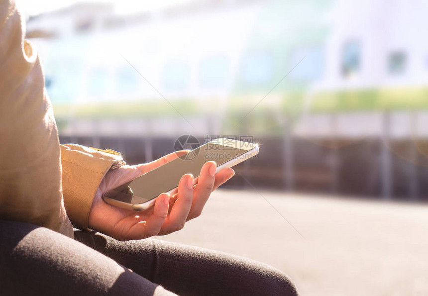 女人在火车站台买票或用手机检查时刻表在模糊的背景下手持智能手机和火车的特写现代图片
