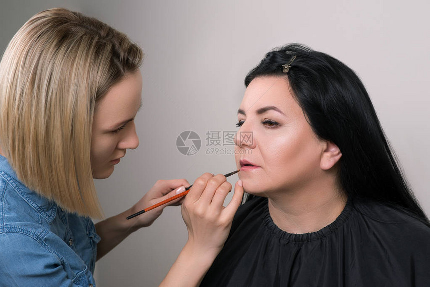 化妆师涂口红美丽的成熟女人在美容院化妆师为迷人的女人化妆在工作室有专业化妆师的图片
