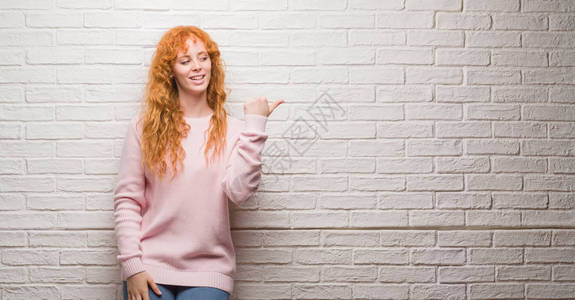 年轻红发女人站在砖墙上图片
