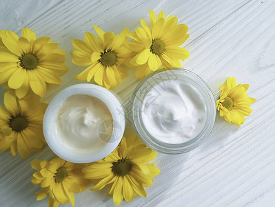 白色木质背景上的奶油色化妆品黄色雏菊花图片