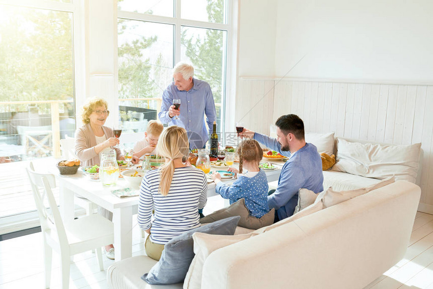 快乐的两代家庭在节日庆祝期间坐在节日餐桌上享用晚餐享用美味佳肴和举杯的广角肖图片