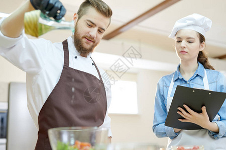 两名专业厨师在餐厅厨房一起做饭和调味沙拉的低角度肖像图片