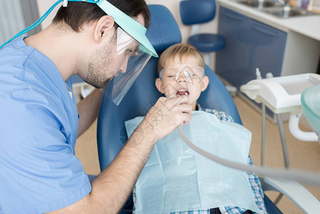 现代诊所牙医治疗小男孩牙齿坐在牙科椅填充蛀牙和专图片