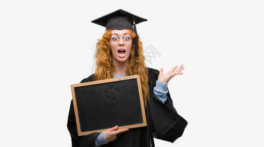 穿着毕业制服的年轻红发女学生拿着黑板非常高兴和奋高清图片
