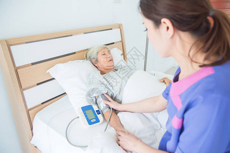护士检查在床上睡觉的高级女病人的血图片