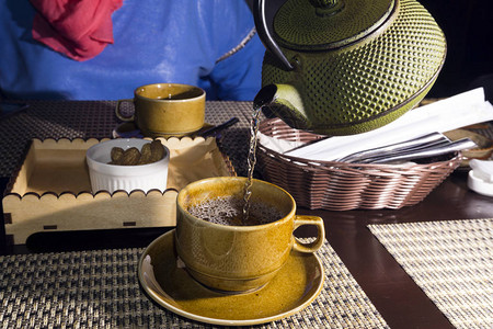 用破旧的铸铁水壶把绿茶倒进杯子里图片