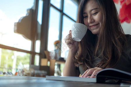 一位美丽的亚洲女在现代咖啡馆喝热咖啡时阅读一本书图片