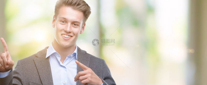 英俊的金发年轻商人笑着看镜头用两只手和指对着另一边图片