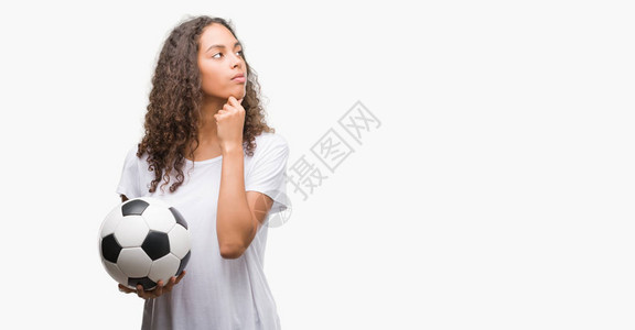 年轻的西班牙裔女拿着足球认真的脸思考问题背景图片