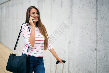 妇女走在车站时携带行李并使用智能电话单图片