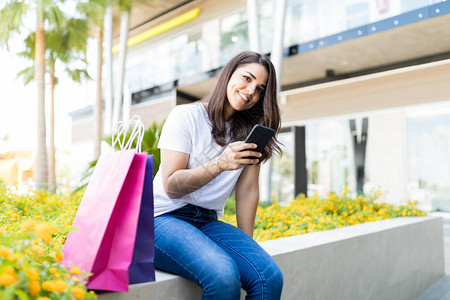 在商场外移动电话上微笑的购物中心妇女社交网络图片