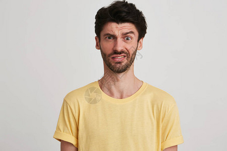 令人惊讶的不高兴的年轻人的肖像带着布里斯特尔戴黄色T衬衫看起来不满意图片