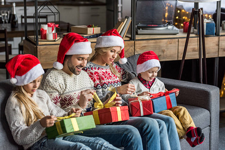 带着圣诞礼帽的幸福家庭开着圣诞节礼物坐在家图片