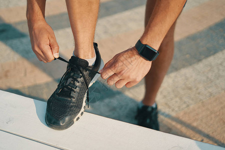 运动员系他的黑色运动鞋运动男子在准备跑步时系鞋带左手智能手图片