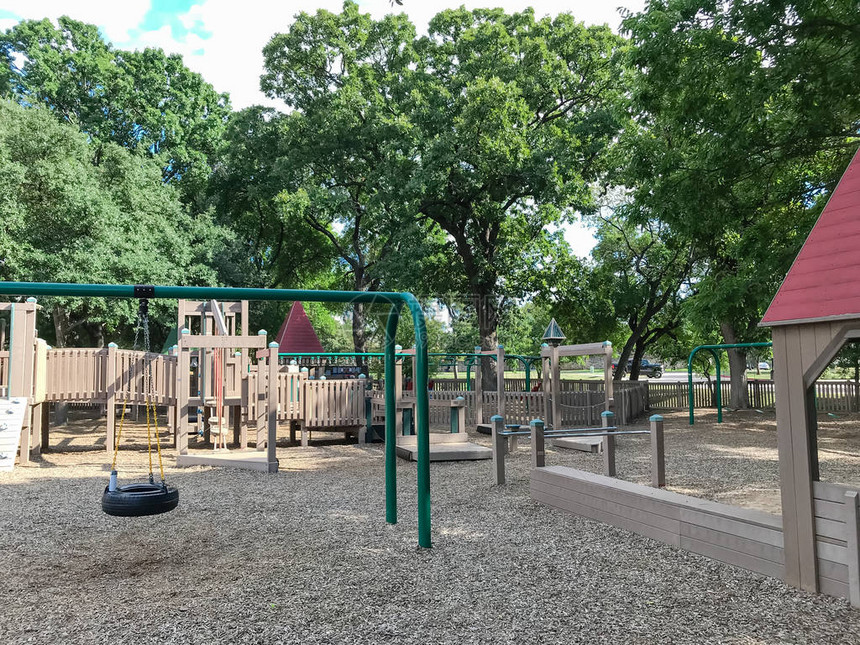 美国得克萨斯州科佩尔市大树茂盛的公共木制儿童游乐场设置了轮胎和椅子秋千夏叶绿云蓝天环绕的图片
