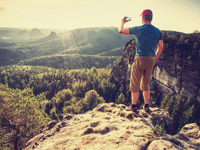 业余爱好者用智能手机在岩石峰上拍照图片