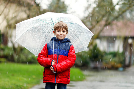 漂亮的小男孩在上学的路上在雨夹雪雨雪中行走背景图片