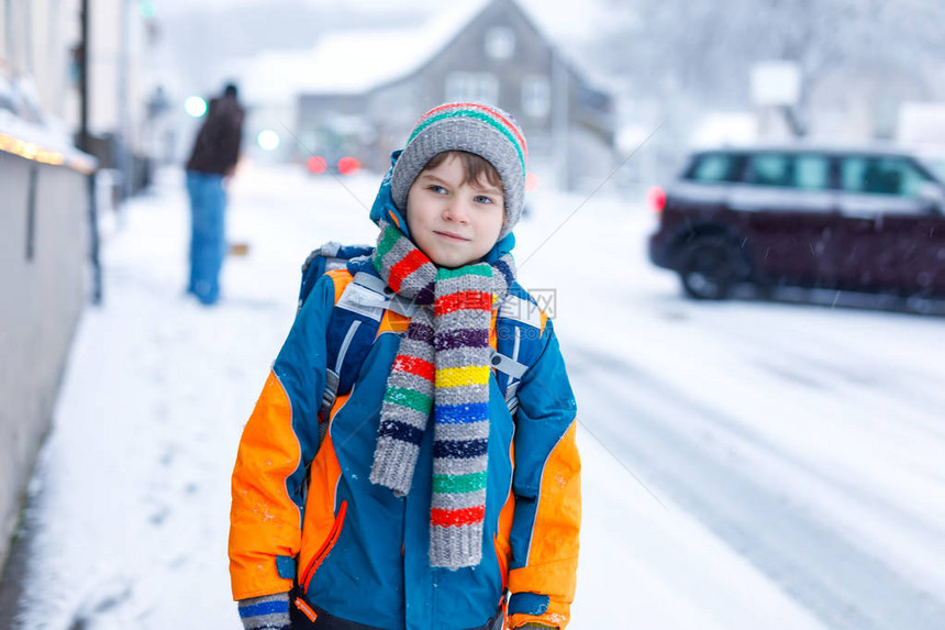 小学生在降雪期间步行去学校的小学男孩城市的清晨和白雪皑的街道学生背着包或书包图片
