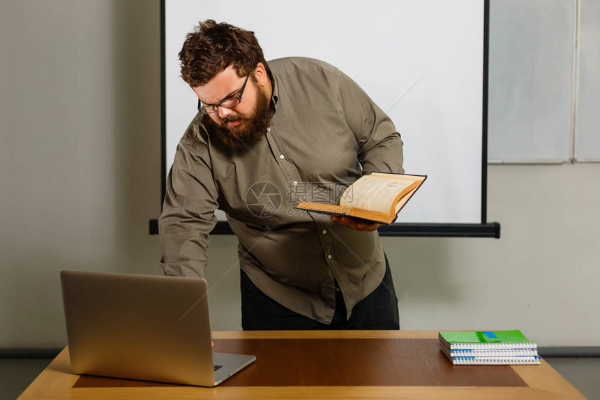 带书和笔记本的有照片的成人教师在桌子上用笔记本电脑工图片