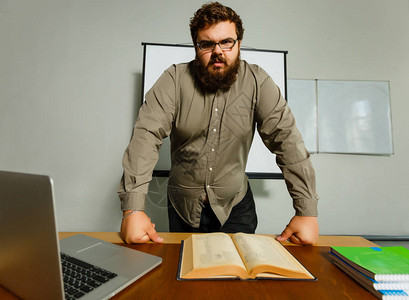 严肃的大胡子教授的肖像与书和笔记本电脑背景图片