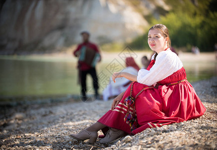 一个穿着俄罗斯国服的女孩坐在沙滩上在阳光中惊人的风景背景图片
