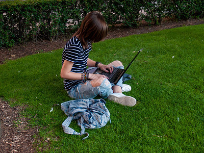 一名少女在大学校园的公园里坐在草地上用笔图片