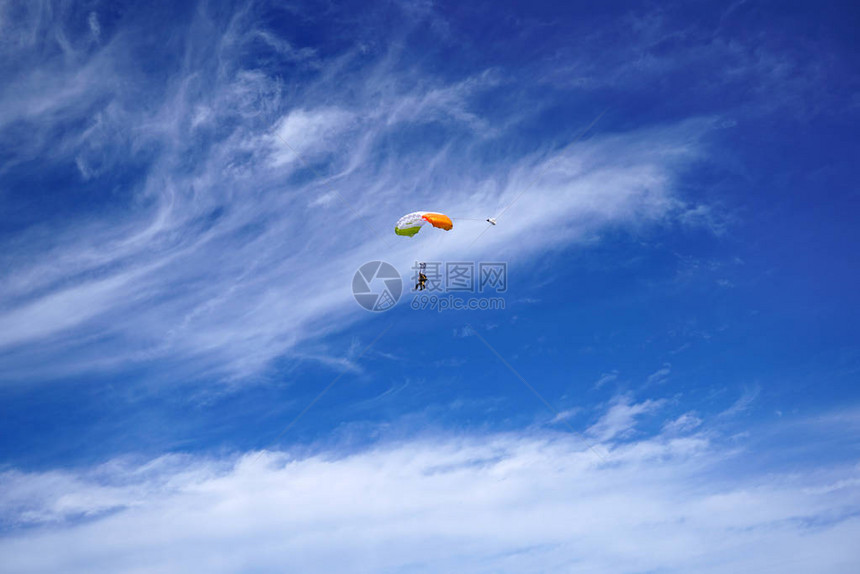 明亮的白色降落伞机盖和串联的跳伞者以不寻常的美丽云彩和蓝天为背景与乘客串联的主人正在飞图片