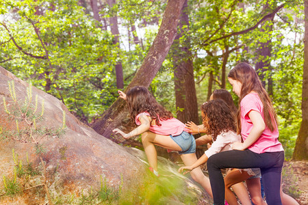 一群小女孩在森林中一个接一个地爬到岩石上图片
