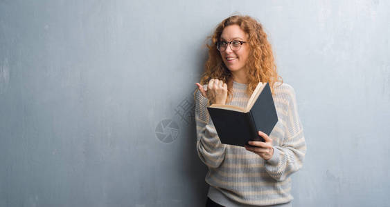 年轻的红头发女人在灰色的格朗基墙上读一本书背景图片