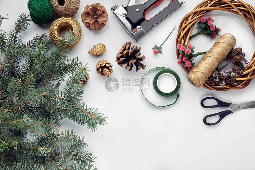 为圣诞节或假期做准备白桌背景上的毛树枝花圈绳索剪刀工艺纸平铺顶视图复制空图片
