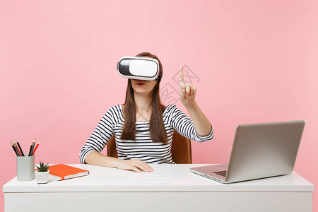 头戴虚拟现实耳机的女孩在头上触摸类似按下钮或指向浮动虚拟屏幕的东西图片