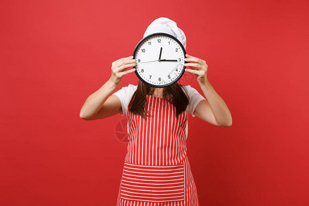 家庭主妇女厨师或面包师穿着条纹围裙白色t恤无边帽厨师帽隔离在红墙背景女人手里拿着前脸圆形时钟快点模拟背景图片