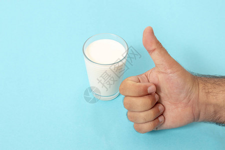 手为蓝色背景上的一杯牛奶竖起大拇指图片