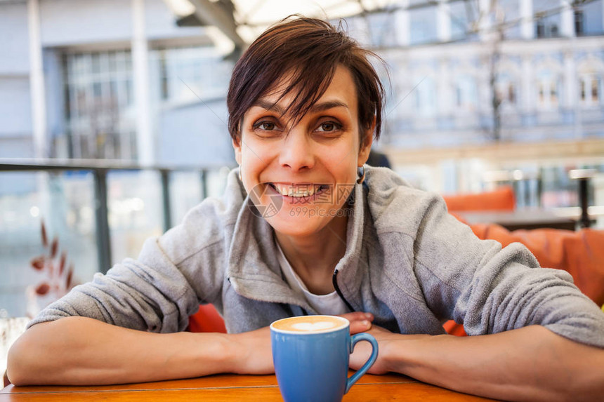 早晨在蓝色杯子里提神饮料微笑的女孩在咖啡店里喝咖啡一名年轻女子正坐在咖啡馆的一张桌子旁一个美丽的黑图片