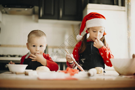 穿着圣诞帽子的可爱男孩和可爱女孩站在厨房桌边图片