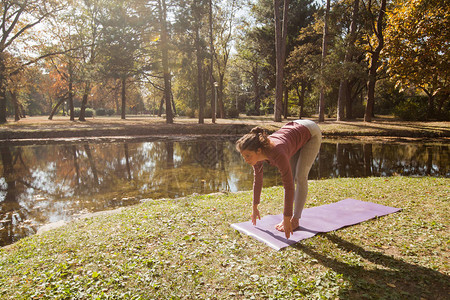 年轻女子在湖边公园运动垫上做瑜伽在美图片