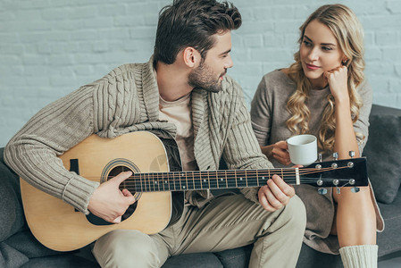 迷人的年轻男人在家为女友弹吉他图片