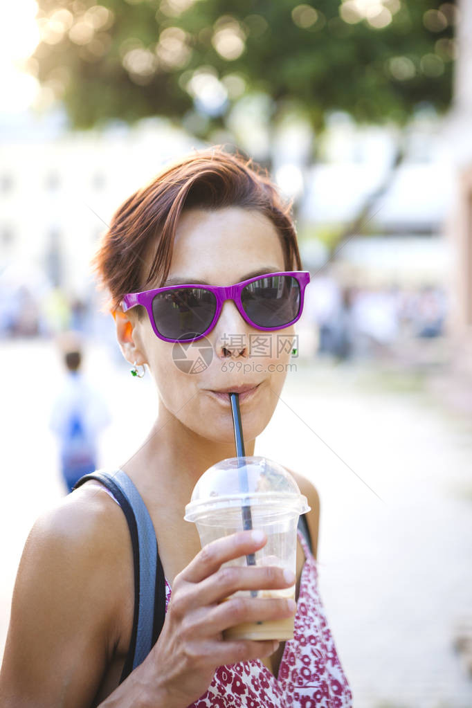 一个女孩用吸管喝饮料一个戴眼镜的女人在城市街道上喝早间咖啡一个微笑的黑发女人从一个塑料