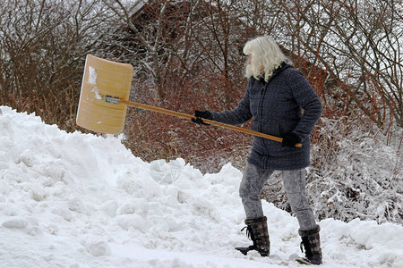 一个女人在冬天下铲雪在雪瀑背景图片