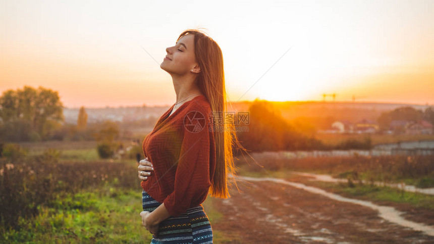 美丽浪漫是怀孕的女孩户外享受大自然抱着她的肚子美丽的秋天模型在日落的光芒中的质夕阳下的阳光浪漫怀图片