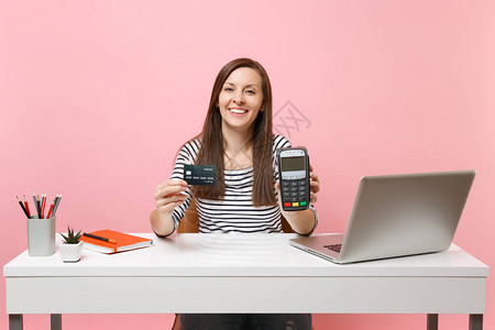 拿着无线现代银行支付终端的女孩在办公桌前处理和获取信用卡支付工作图片