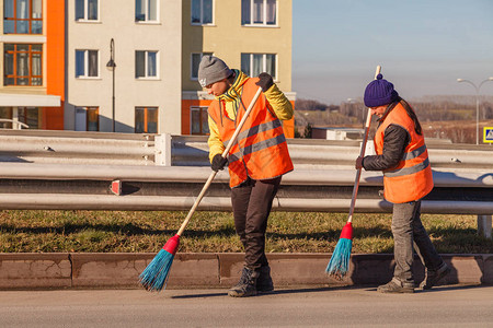 穿着制服的清洁工拿着铁锹和扫帚清扫道路上的树叶和杂物冬季前清洁城市户外工作和城背景图片