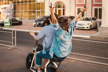 可爱的年轻夫妇在夏天驾驶电动自行车在现代城市约会和交通方图片